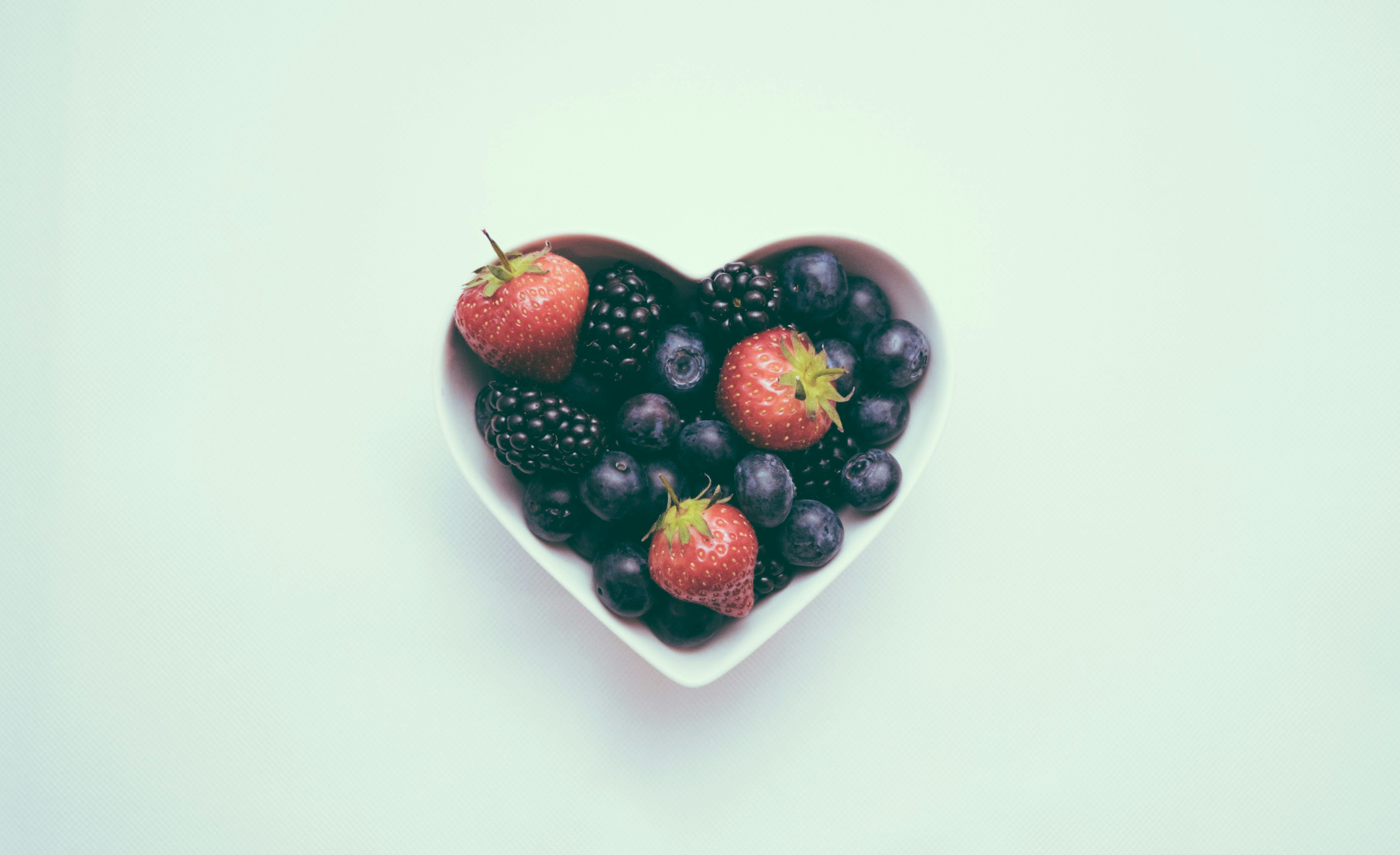 Bol en forme de cœur rempli de fruits rouges et de myrtilles, symbolisant une alimentation saine et bénéfique pour la santé.